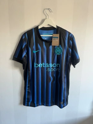 Inter Milan matchtröja Nike svart/blå - Snygg Inter Milan matchtröja från Nike i svart och blått med vertikala ränder. Tröjan har klubbmärke och Nike-logga i ljusblått samt sponsortryck på bröstet. Tillverkad i lätt och ventilerande material, perfekt för fotboll eller träning.