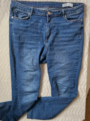 Blå skinny jeans från Vero Moda - Säljer ett par blå skinny jeans från Vero Moda med klassisk femficksmodell och snygga slitningar framtill. Jeansen har normalhög midja, dragkedja och knappstängning samt kontrastsömmar. Perfekta för en trendig och avslappnad look.