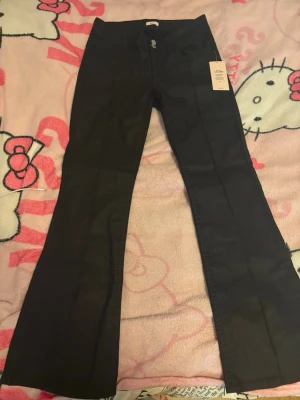 Svarta bootcut jeans med hög midja - Snygga svarta bootcut jeans med hög midja och klassisk femficksdesign. Jeansen har utsvängda ben och stängs med dragkedja och knapp framtill. Perfekta för dig som gillar en retroinspirerad look. Materialet ser ut att vara stretchigt för extra komfort.