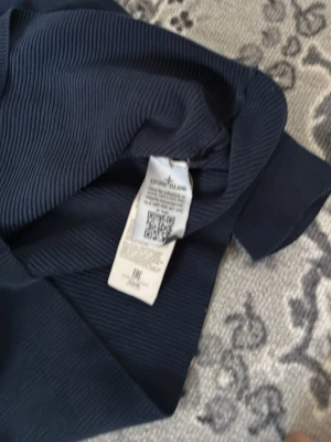 Mörkblå stickad tröja Stone Island - Snygg mörkblå stickad tröja från Stone Island med klassisk patch på ärmen. Tröjan har rund halsringning, lång ärm och ribbad struktur som ger en modern look. Perfekt för dig som gillar streetwear och vill ha något stilrent i garderoben.