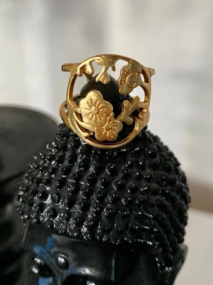 Pilgrim guldpläterad  ring med blommönster - Unik guldfärgad ring med ett detaljerat blommönster i fronten. Ringen har en öppen design och är tillverkad i metall med en elegant, rundad form. Perfekt present, justerbar storlek.