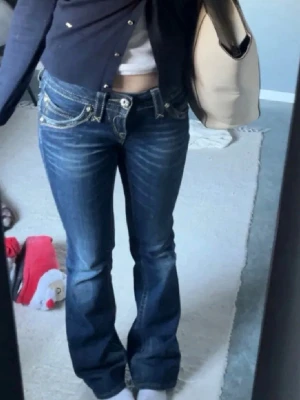 Blåa bootcut jeans från Rock Revival - Säljer ett par blåa bootcut jeans från Rock Revival. Jeansen har låg midja, slitningar framtill och super fin mörkblå färg. Tyvärr kommer inte jeansen till användning för mig❣️pris kan diskuteras 