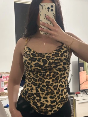 Leopardmönstrad linnetopp med guldkedjor - Snygg leopardmönstrad linnetopp med tunna guldfärgade kedjeband. Toppen har en figurnära passform och lätt draperad ringning framtill. Perfekt för dig som vill sticka ut och addera lite edge till din outfit. Storlek S