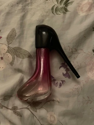Parfymflaska formad som högklackad sko - Unik parfymflaska i form av en högklackad sko med svart klack och lock samt rosa till genomskinlig glasflaska. Flaskan har en elegant och modern design som sticker ut på sminkbordet. Finns halva av flaskan kvar