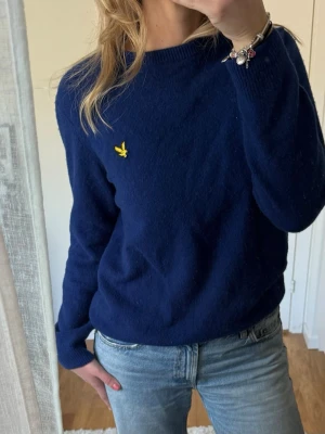 Mörkblå stickad tröja från Lyle & Scott - Mörkblå stickad tröja från Lyle & Scott med rund halsringning, långa ärmar och ribbstickade muddar vid ärmslut och nederkant. Perfekt både till mer casual och uppklätt!