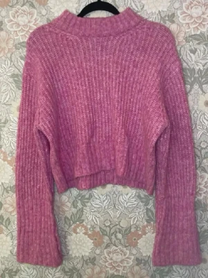 Rosa croppad stickad tröja - Mysig rosa stickad tröja med croppad passform och breda, långa ärmar. Tröjan har en hög krage och är ribbstickad i ett mjukt material, perfekt för kyliga dagar. Inget synligt märke.