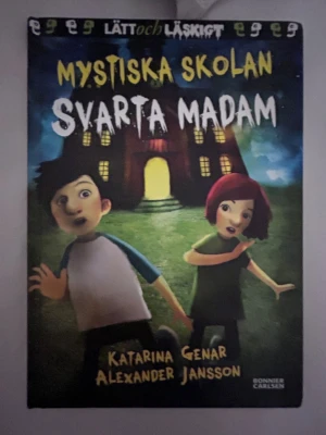 Mystiska skolan: Svarta Madam - En spännande och lättläst bok med titeln 'Mystiska skolan: Svarta Madam' av Katarina Genar och Alexander Jansson. Omslaget är färgstarkt med illustrationer av två barn framför en mystisk skola i mörka toner. Perfekt för dig som gillar rysliga äventyr.Lätt läst