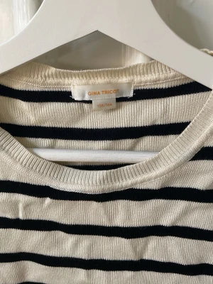 Randig t-shirt från Gina Tricot - Snygg randig t-shirt från Gina Tricot i vitt och svart. T-shirten har korta ärmar, rund halsringning och är gjord i mjuk bomull. Något kort så den ger liiiite ”magtröja” vibbar. 