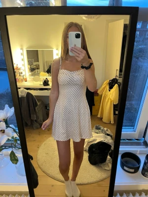 Beige prickig kort klänning - Söt beige kort klänning med bruna prickar och tunna axelband. Klänningen har en lätt utsvängd passform och är perfekt för varma dagar. Materialet känns lätt och luftigt, vilket gör den skön att bära. Enkel men trendig design som passar till många tillfällen.