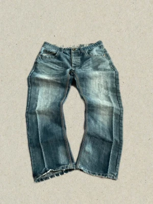 Blå slitna jeans - Säljer ett par blå jeans med tydlig slitning och tvättade detaljer. Jeansen är baggy och har en japansk stil. Materialet är denim i bomull och de har en avslappnad passform. Perfekta för en cool och avslappnad stil. 