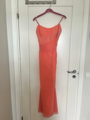 Lång korallfärgad klänning med pärlor - Elegant långklänning i korall med smala axelband och vacker pärl- och paljettbrodyr över bysten. Klänningen har figurnära passform och lätt drapering vid midjan. Jättefin till bal eller annan fest! Passar 34-36. Köpt för 3000kr. Nyskick! 