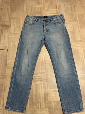 Blå raka jeans i klassisk modell - Säljer ett par blå jeans med rak passform och fem fickor. Jeansen har en klassisk tvättad look och är tillverkade i denim. Perfekta för dig som gillar en enkel och tidlös stil. Passar till det mesta och har en skön midjehöjd.