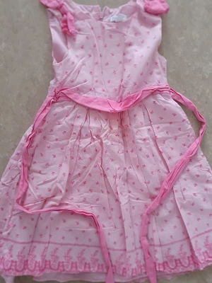 Klänning - Söt ljusrosa klänning från Charter Club med små rosa blommor och dekorativt band i midjan. Klänningen har ärmar med rosett och broderade detaljer längst ner. Tillverkad i bomull med foder i polyester och bomull.