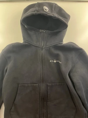 Svart hoodie från Sail Racing🖤 - Svart hoodie från Sail Racing med dragkedja framtill och två stora fickor. Klassisk huva med logga på toppen och diskret Sail Racing-tryck på bröstet. Tillverkad i mjukt material som känns skönt mot huden. Storlek 170 men passar mig som har storlek s-m! Skulle säga att det är en tjejigare modell