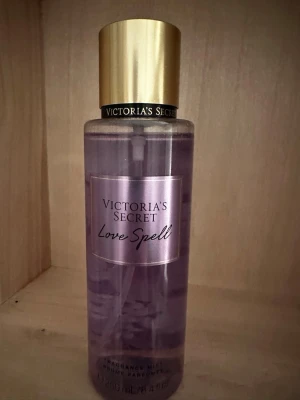 Victoria's Secret Love Spell parfym - Victoria's Secret Love Spell parfym med lila vätska i en cylinderformad plastflaska. Flaskan har en elegant guldfärgad kork och en etikett i ljuslila med svart text. Doften är fräsch och feminin, perfekt för dig som gillar söta och blommiga toner.