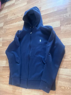 Ralph lauren hoodie (snälla köp behöver pengar för peptider) - Mörkblå hoodie med dragkedja från Polo Ralph Lauren. Klassisk design med huva, två fickor framtill och vit broderad logga på bröstet. Perfekt för en avslappnad och stilren look.