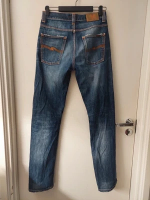 Blå Nudie Jeans - Säljer ett par riktigt feta o trendiga blå jeans från Nudie Jeans med raka ben och snygga slitningar.  Tillverkade i denim med en autentisk tvättad look som är riktigt trendigt nu. Storlek: 31/34 Skick: Mycket bra! Bara att skriva om du har några frågor samt prisförslag eller vill ha mått på byxorna!🙌