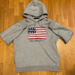 Unika Ralph Lauren Hoodie - Säljer en unik grå hoodie från Ralph Lauren med klassisk flaggdesign. Storlek M. Mycket bra skick utan skador. QR-kod finns som äkthetsbevis.