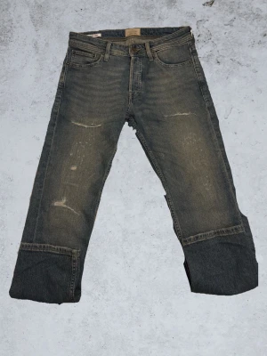 Grå slitna jeans - Säljer ett par grå jeans med slitningar från Jack & Jones. Stilrena och perfekt för skolan andra tillställningar. Hojta till för frågor!