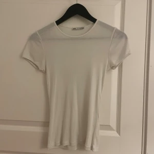 Vit t-shirt från Zara - En klassisk vit t-shirt från Zara med rund halsringning och korta ärmar. Modellen är figurnära och enkel, perfekt att matcha med allt. Tillverkad i mjukt bomullsmaterial för en skön känsla. Storlek XS-S