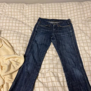 Wrangler Sofia bootcut jeans blå W27 L34 - Snygga blå bootcut jeans från Wrangler, modell Sofia. Klassisk femficksdesign med kontrastsömmar och läderpatch på bakfickan. Jeansen har en något utsvängd passform nertill och är tillverkade i slitstarkt denimtyg. Perfekta för dig som gillar en tidlös look.