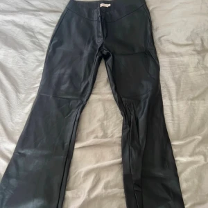Svarta bootcut byxor i skinnimitation Nelly - Snygga svarta byxor från Nelly i skinnimitation med bootcut-modell. Byxorna har hög midja, dragkedja och knapp framtill. Perfekta för dig som vill ha en edgy look med lite extra attityd. En knapp saknas