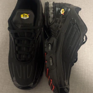 Nike skor - Säljer ett par Nike Air Max Plus Tn sneakers i helsvart med röda detaljer på sulan och tydliga Tn-loggor. Skorna har en chunky sula med synlig Air Max-dämpning och coola linjer på ovandelen. Perfekta för dig som gillar streetwear och vill sticka ut.                            Jag har limat skorna men syns knappt              