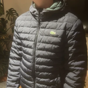 Mörkblå pufferjacka från Lacoste - Snygg mörkblå pufferjacka från Lacoste med huva och dragkedja. Jackan har det klassiska Lacoste-krokodilmärket på bröstet och är quiltad för extra värme. Perfekt för kyliga dagar och har en clean, sportig look. Mörkgrön på insidan. Pm för fler bilder eller info :)