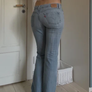 Levis ljusblå bootcut jeans - Ljusblå Levis jeans med klassisk bootcut-passform och låg midja. Jeansen har fem fickor, bälteshällor och dragkedja. Tillverkade i mjukt denim med en lätt tvättad look och subtila slitningar. Jag har sytt in dem i midjan på ena sidan för en snyggare passform men det går enkelt att sprätta upp! Innerbenslängden är 80 cm och midjemåttet mätt rakt över är 38 cm.  