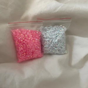 Rosa och silvriga diamantpärlor  - Två påsar med glittrande ansiktsstenar i rosa och silver. Perfekta för att skapa kreativa sminklooks eller festivalmakeup. Stenarna är runda och platta, lätta att applicera med lim för extra effekt på ögon eller kinder.