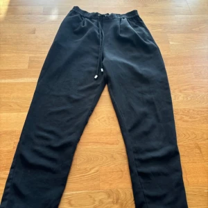 Svarta byxor med snörning - Svarta byxor med elastisk midja och snörning framtill. Byxorna har raka ben. 