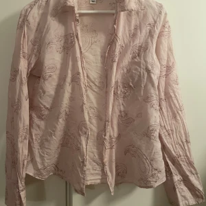 Ljusrosa skjorta med paisleymönster, H&M  - Ljusrosa skjorta från H&M med paisleymönster i en mörkare rosa ton. Skjortan har klassisk krage, långa ärmar och knäppning framtill. Tillverkad i mjuk bomull som känns skön mot huden. Perfekt för dig som gillar en chill och trendig look. Stl 42 