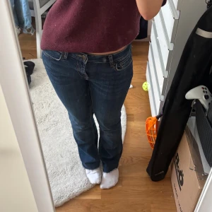 Lågmidjade jeans - Säljer ett par mörkblå jeans med bootcut-modell och låg midja. Jeansen har klassisk femficksdesign, dragkedja och knapp framtill. Snygg passform som sitter tajt upptill och släpper ut vid bensluten. Perfekta till sneakers eller boots.