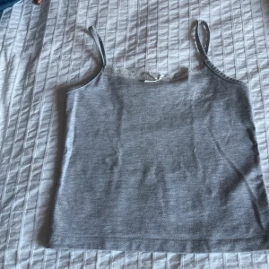 Grå linnetopp med spets från Gina Tricot - Supersöt grå linnetopp från Gina Tricot med tunna axelband, vit spetskant och liten rosett framtill. Tryck med texten 'J'adore' och hjärta på bröstet. Perfekt till jeans eller kjol för en chill look. 💖💖