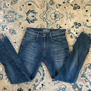 Blå jeans Grant modell 521 - Snygga blå jeans från Grant, modell 521, med klassisk femficksdesign och diskret slitning framtill. Jeansen har raka ben och normal passform, tillverkade i tåligt denimtyg. Perfekta för dig som gillar en enkel och stilren look.