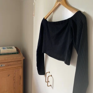 Svart ribbad offshoulder topp NLY One - Säljer en svart croppad offshoulder topp från NLY One i storlek M. Toppen är ribbad och har långa ärmar, perfekt för att skapa en snygg och trendig look. Materialet är mjukt och stretchigt för en bekväm passform. Använd 1 gång✨