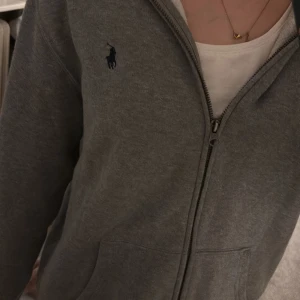 Grå hoodie från Polo Ralph Lauren XL - Mysig grå hoodie från Polo Ralph Lauren .Tröjan har dragkedja framtill, huva och två fickor. Klassisk broderad logga på bröstet och långärmad modell. Är lite oversized men skulle nog säga att storleken är s/m 