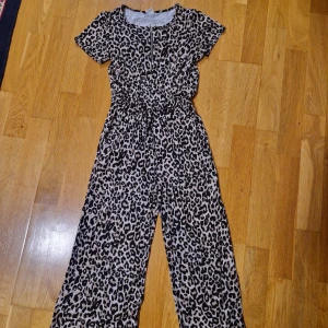 Leopardmönstrad byxdress från Lindex - Cool byxdress från Lindex i leopardmönster med dragkedja framtill och snörning i midjan. Mjuk och skön känsla, kortärmad och vida ben. Storlek 128 men kan bäras länge eftersom benlängden inte måste vara hellång i denna modellen.