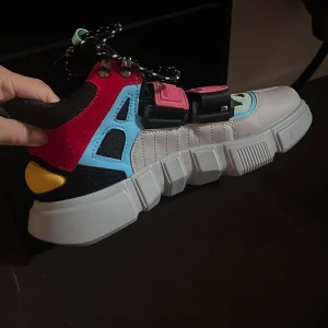 Färgglada chunky sneakers med detaljer - Säljer ett par riktigt unika chunky sneakers i flera färger: vit, svart, röd, blå, gul och mintgrön. Skorna har coola detaljer som breda rosa spännen, svartvita snören och en rejäl platt sula. Materialmix av syntet och textil, perfekt för dig som vill sticka ut.