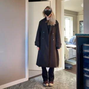 Mörkbrun lång kappa med bälte - Säljer en mörkbrun kappa med bälte i midjan. Perfekt för dig som vill ha en stilren och klassisk look under höst och vinter.