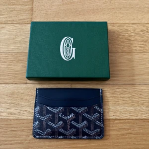 Goy4rd plånbok - Exklusiv korthållare från Goy4rd i svart och brunt med ikoniskt mönster och vita detaljer. Slimmad design med flera kortfack och klassisk Goy4rd-logga framtill. Tillverkad i skinn och levereras med originalask och certifikat.