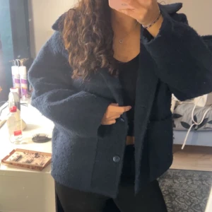 Mörkblå kappa med knappar - Säljer en mörkblå teddyjacka med oversized passform och stora knappar framtill. Jackan har en fluffig textur, bred krage och långa ärmar. Perfekt för dig som vill ha en mysig och trendig look.