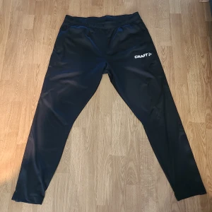 Svarta träningsbyxor från Craft - Svarta träningsbyxor från Craft, storlek XL. Byxorna har dragkedja vid benslut. Tillverkade i syntetmaterial som andas.