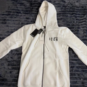 Dsquared2 Zip - Snygg vit hoodie från Dsquared2 med svart 'ICON'-tryck på bröstet. Tröjan har huva med dragsko, hel dragkedja framtill och två stora fickor. Tillverkad i mjuk bomull, perfekt för en clean och trendig look.
