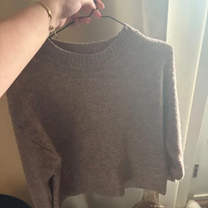 Beige stickad tröja med rund hals - Mysig beige stickad tröja med rundad hals och långa ärmar. Tröjan har en enkel, loose passform och ribbad kant vid halsen. Perfekt för att hålla sig varm och chill under kyliga dagar.