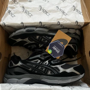 Asics GEL-NYC graphite grey/black - Säljer ett par snygga Asics sneakers i svart och grå med coola detaljer och meshpaneler för extra ventilation. Skorna har snörning och en platt sula som ger skön komfort. Perfekta för dig som gillar sportig stil och vill ha något som sticker ut. FÖRSÖK INTE PRUTA JAG SVARAR INTE.