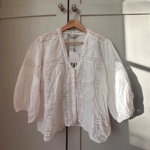 Vit spetsblus från Zara, storlek Xs/S - säljer en superfin vit blus från Zara med v-ringning och trekvartsärmar. Blusen har vackra spetsdetaljer och broderade partier framtill och på ärmarna. Luftig och lätt i bomull, perfekt för vår och sommar. Är i storlek S men skulle säga att de är mer Xs/S. Säljs med originaltag kvar så är helt ny. Nypris går för 300 kr men säljer för 150 kr