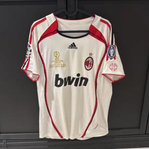 AC Milan Maldini Champions League tröja - AC Milan fotbollströja från Champions League-finalen 2007 med Maldini och nummer 3 på ryggen. Vit med röda och svarta detaljer, broderade märken och Bwin-tryck på bröstet. Korta ärmar, tillverkad i lätt och ventilerande material. Har även en liten fläck på backsidan