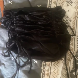 Svart sammetskjol med snörning Divided XS - Supersnygg svart sammetskjol från Divided i storlek XS. Kjolen är kort och har trendiga snörningsdetaljer på sidorna som ger en cool rynkad effekt. Materialet är mjukt och glansigt, perfekt för att sticka ut. Elastisk midja för skön passform.