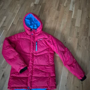 Röd vinterjacka Everest - Röd, varm vinterjacka från Everest med blått foder. Jackan har dragkedja, stora fodrade fickor och en bröstficka med dragkedja. Går justera i midjan och har innerficka. Knappt använd, i nyskick. Syns lite på ena mudden (se bild) men annars inga skavanker😊